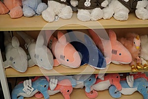 Multi colored shark stuffed children`s toy in a store. Pink plush shark toys on shelf. Lot of toy sharks in market. Lot of plush