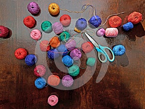 multi-colored skeins of threads and scissors scattered on a dark wooden background,
