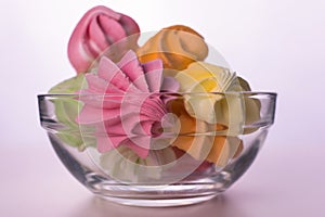 Multi-colored small meringues in a glass transparent plate on a white background.Close-up.