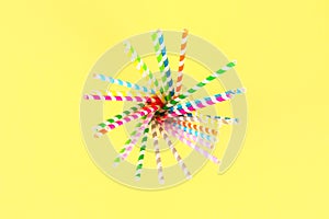 Multi-colored straw paper tubes on a bright yellow pastel background. Top view, copy space.
