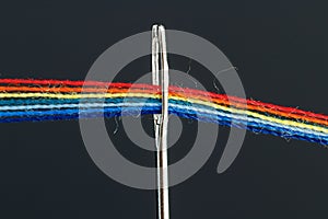 Multi-colored threads for sewing in the form of a rainbow pass through an antique needle on a black background