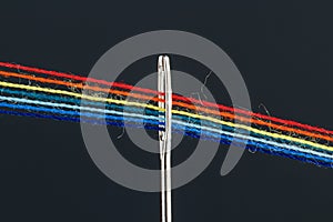 Multi-colored threads for sewing in the form of a rainbow pass through an antique needle on a black background