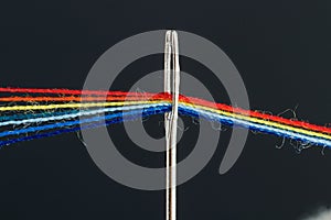Multi-colored threads for sewing in the form of a rainbow pass through an antique needle on a black background