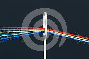 Multi-colored threads for sewing in the form of a rainbow pass through an antique needle on a black background