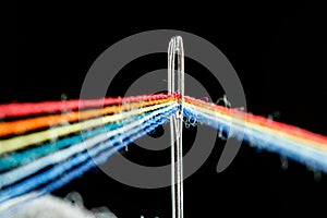 Multi-colored threads for sewing in the form of a rainbow pass through an antique needle on a black background