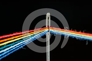 Multi-colored threads for sewing in the form of a rainbow pass through an antique needle on a black background