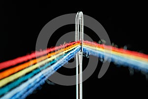 Multi-colored threads for sewing in the form of a rainbow pass through an antique needle on a black background