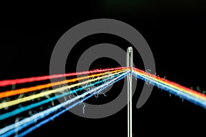 Multi-colored threads for sewing in the form of a rainbow pass through an antique needle on a black background