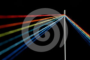 Multi-colored threads for sewing in the form of a rainbow pass through an antique needle on a black background