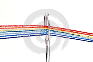Multi-colored threads for sewing in the form of a rainbow pass through an antique needle on a white background