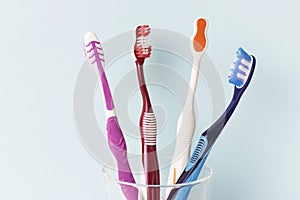 Multi-colored toothbrushes in a glass cup, blue background