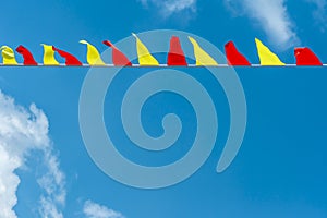 Multi colored triangular flags develop on the background of blue sky. Colorful fairground flags.