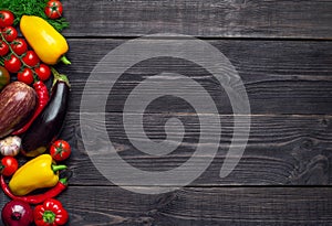 Multi-colored vegetables laid out on the left on a wooden background with empty place for text