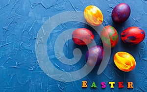 Multi-colored wooden letters making up the words happy easter and decorative colourful eggs on a blue background with copy space