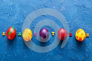 Multi-colored wooden letters making up the words happy easter and decorative colourful eggs on a blue background. Top view