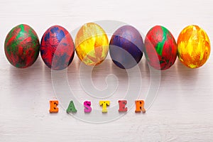 Multi-colored wooden letters making up the words happy easter and decorative colourful eggs on a white background with