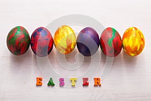 Multi-colored wooden letters making up the words happy easter and decorative colourful eggs on a white background.