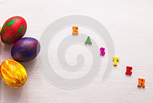 Multi-colored wooden letters making up the words happy easter and decorative colourful eggs on a white background with