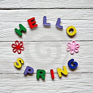 Multi-colored wooden letters making up the words Hello spring and multi-colored wooden flowers on a white wooden background.