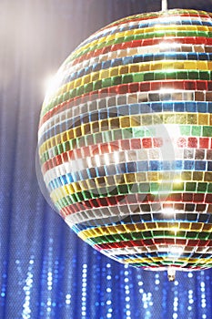 Multi-coloured disco ball in front of blue stage curtain cropped