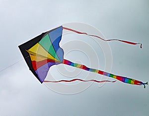 Multi coloured kite with a long tail and two streamers sours high in the sky photo