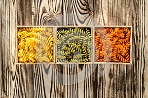 Multi-coloured pasta in the form of spirals lies in square wooden boxes that stand on a table