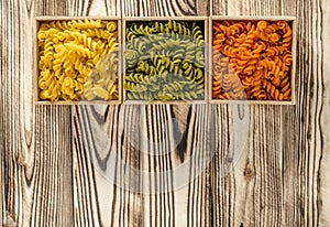 Multi-coloured pasta in the form of spirals lies in square wooden boxes that stand on a table