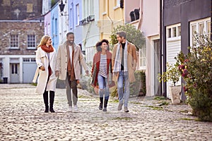 Multi Cultural Couple With Friends Walking Along Residential City Street In Fall Or Winter