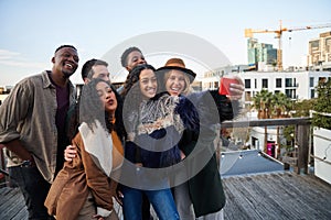 Multi-cultural group of friends taking a selfie at a rooftop party. Posing with young adult friends.