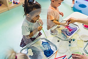 Multi-cultural nursery school. Toddlers playing with striped straws and milk painting, using nontoxic food coloring for