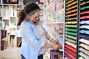 Multi-ethnic beautiful pregnant woman, customer chooses vibrant color paper for design, fine art or painting at art shop