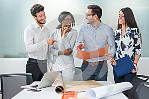 Multi-ethnic business team discussing project or idea while standing near the desk in modern office.