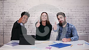 Multi-ethnic business team showing thumb up while sitting at the table in modern office. Slowmotion shot