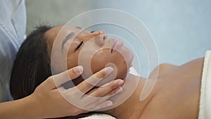 Multi ethnic calm young woman is getting medical face massage from professional hand.