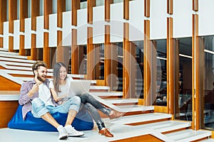 Multi-ethnic college student couple celebrate together with laptop on stairs in university campus or modern office