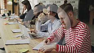 Multi-ethnic concentrated team of coworkers working on technology startup project in openspace office. Young hipster man