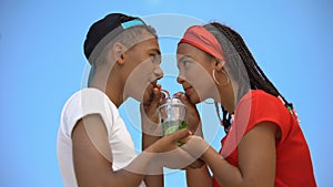 Multi-ethnic couple in love drinking glass of fresh cocktail through two straws