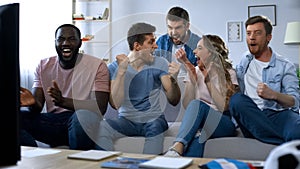 Multi-ethnic friends celebrating goal, watching football at home, togetherness