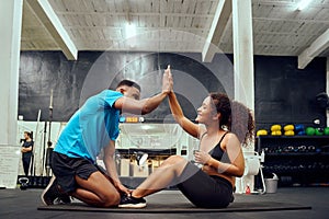 Mixed race friends doing cross fit in the gym. African American male encouraging African American female during sit-ups