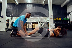 Mixed race friends doing cross fit in the gym. African American male encouraging African American female during sit-ups