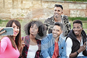 Multi-ethnic friends smiling while taking a selfie with a mobile phone together outdoors.