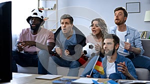 Multi-ethnic German fans sitting on sofa and watching game, supporting team