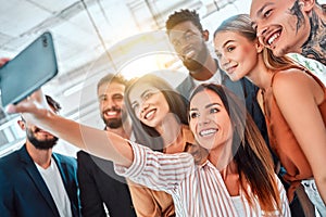 Multi-ethnic group of adult people smiling at camera while taking selfie photo in office