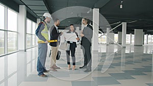 Multi-ethnic group of businesspeople talking and studying blueprint indoors in modern commercial building