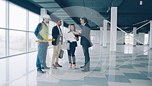 Multi-ethnic group of businesspeople talking and studying blueprint indoors in modern commercial building