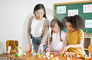 Multi-ethnic group of children school standing and playing with colorful blocks on table with Female Asian teacher in classroom.