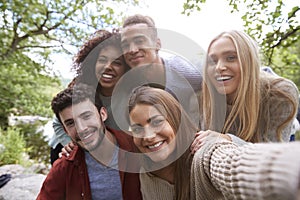 Multi ethnic group of five young adult friends pose to camera while taking a selfie during a break in a hike