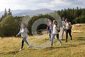 A multi ethnic group of five young adult friends smile while walking on a rural path during a mountain hike, side view