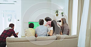 Multi ethnic group of friends chatting while sitting on the sofa in a spacious living room and watching a football match