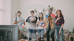 Multi ethnic group of friends listening and singing French national anthem before watching sports championship on TV